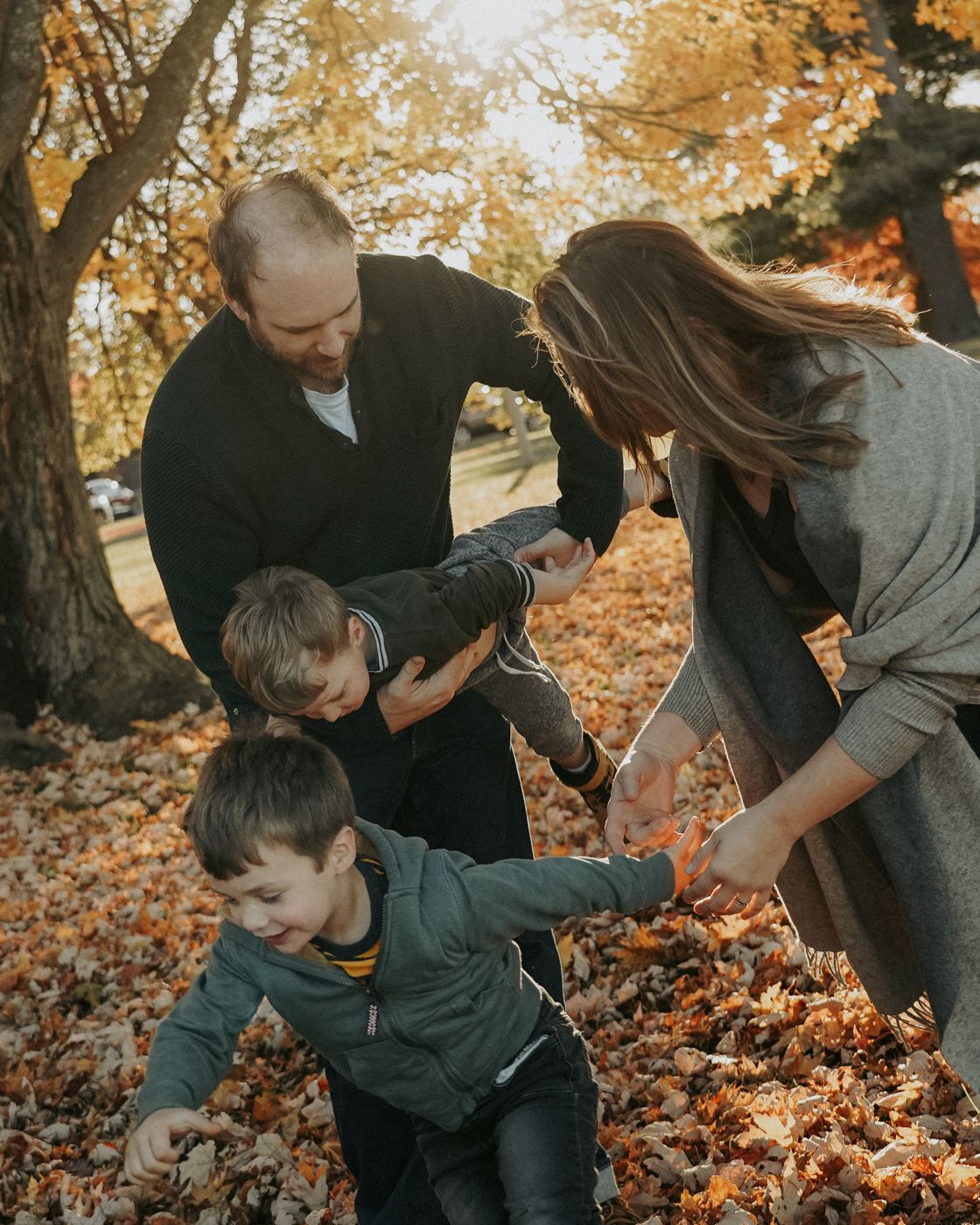 Parents playing with their two boys in golden fall leaves