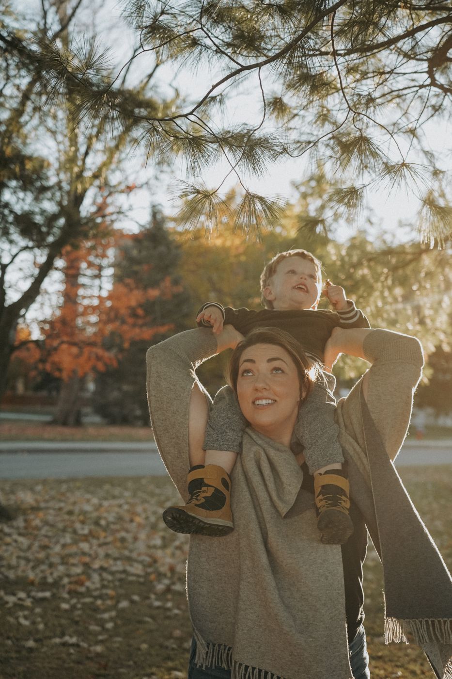 Mom carrying her little boy on her shoulders under a pine in golden light