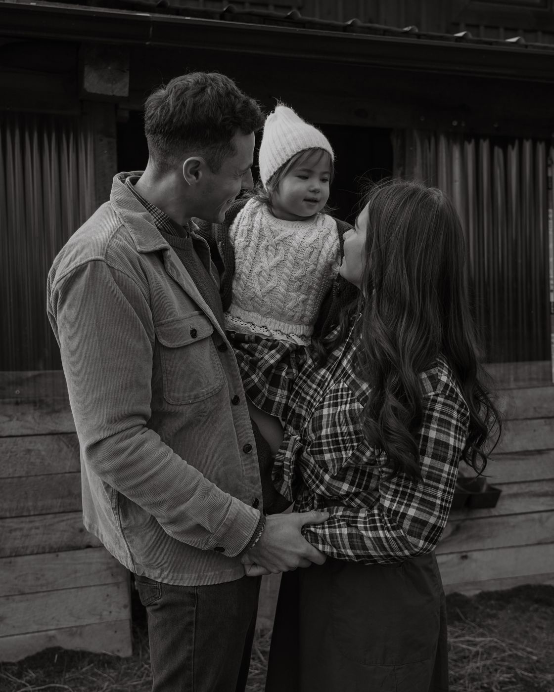Black and white photo of parents holding their daughter by the barn