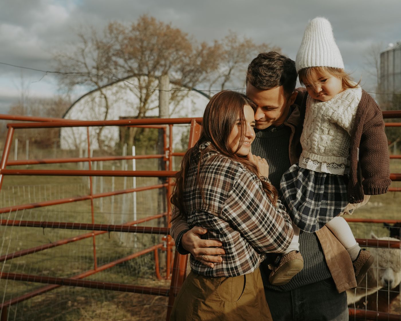 Family embracing by a red farm gate in soft evening light