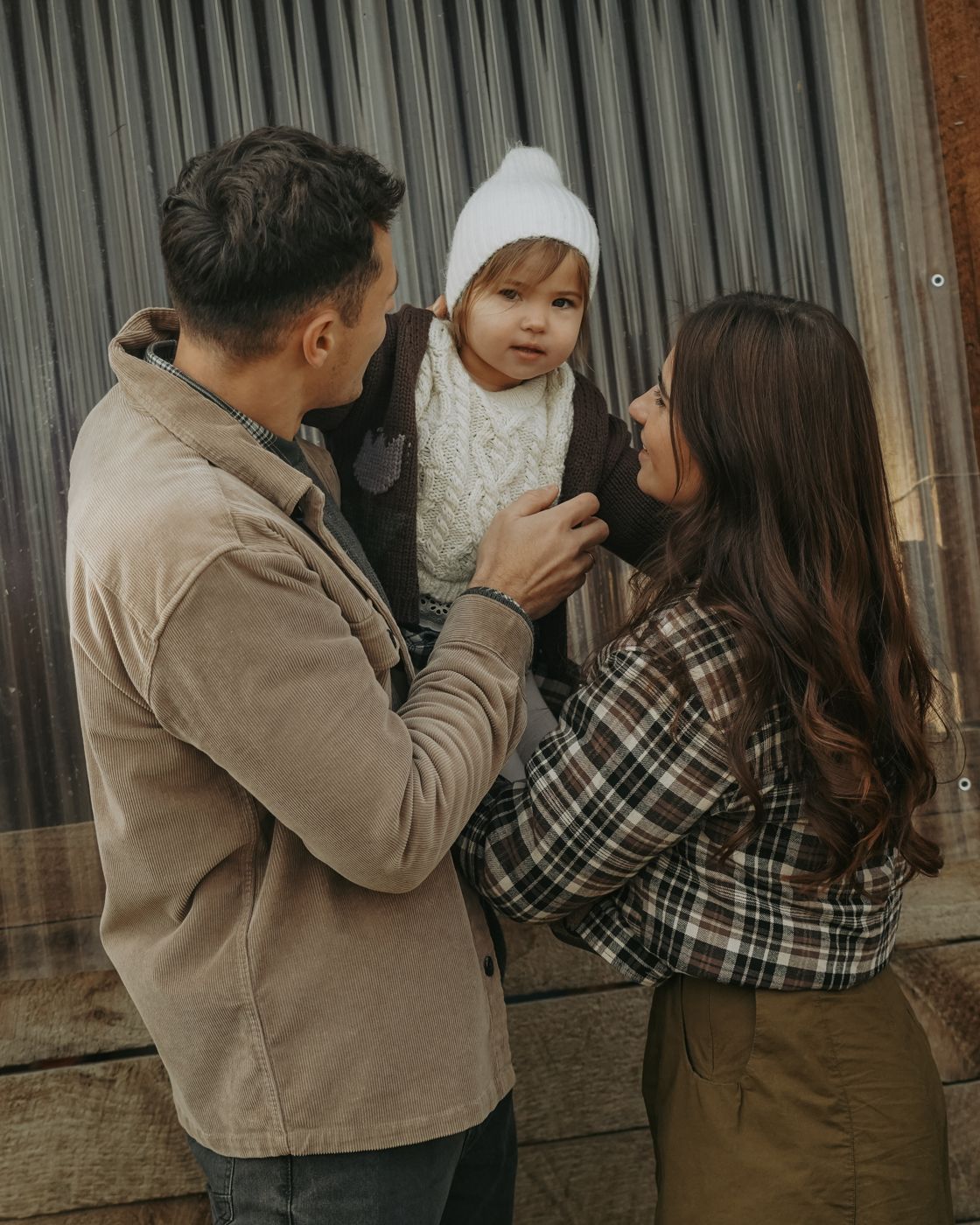 Parents lifting their daughter in front of a metal barn wall