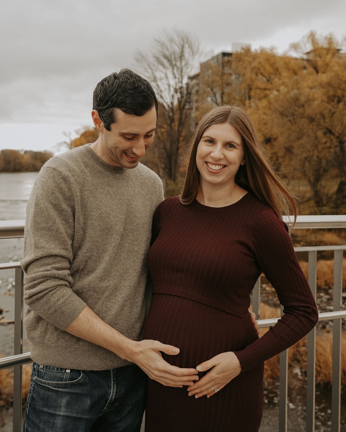 Smiling expecting couple on a bridge by the river