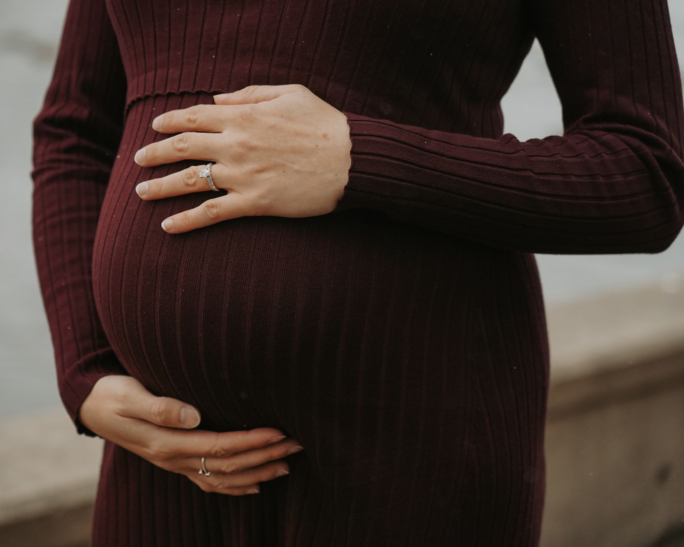 Close-up of hands cradling a baby bump in a burgundy dress