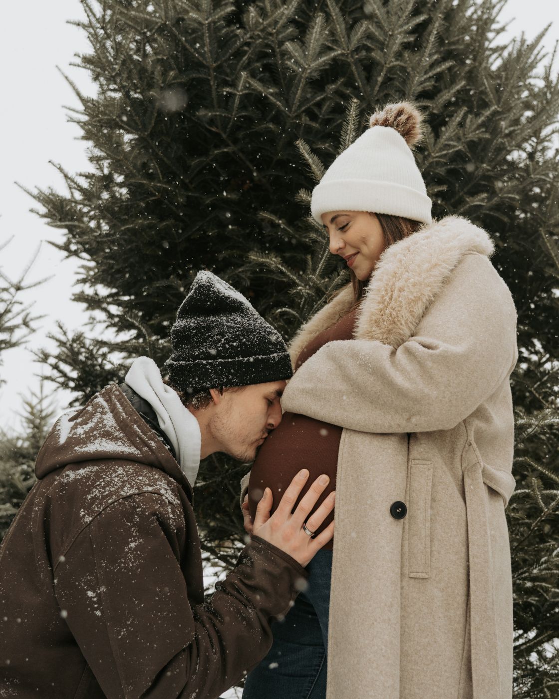 Partner kneeling to kiss the baby bump as snow falls