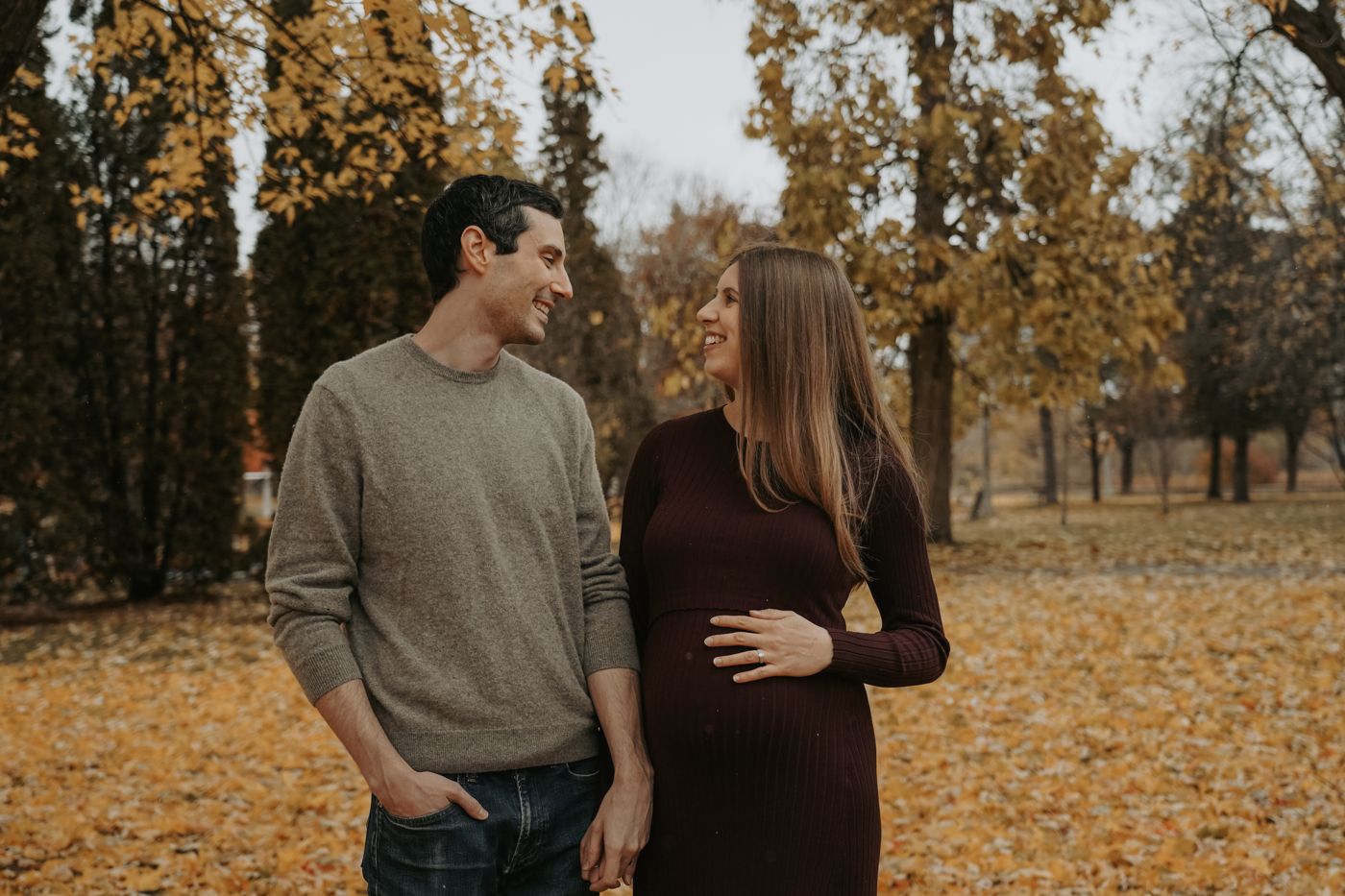 Expecting couple smiling at each other among golden fall leaves