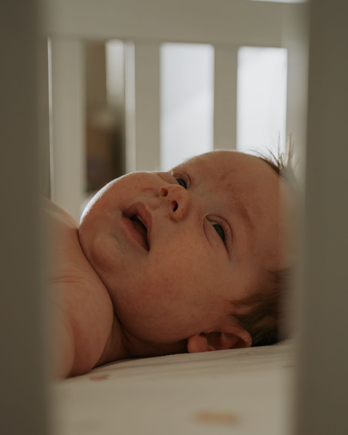 Newborn face seen through the crib bars