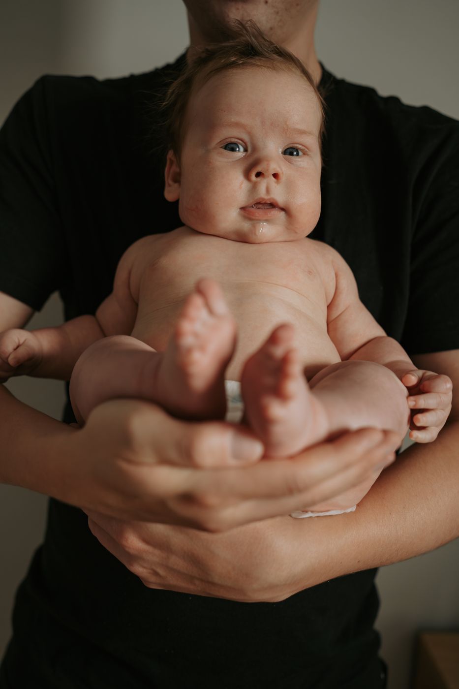 Baby held in dad's arms looking at the camera