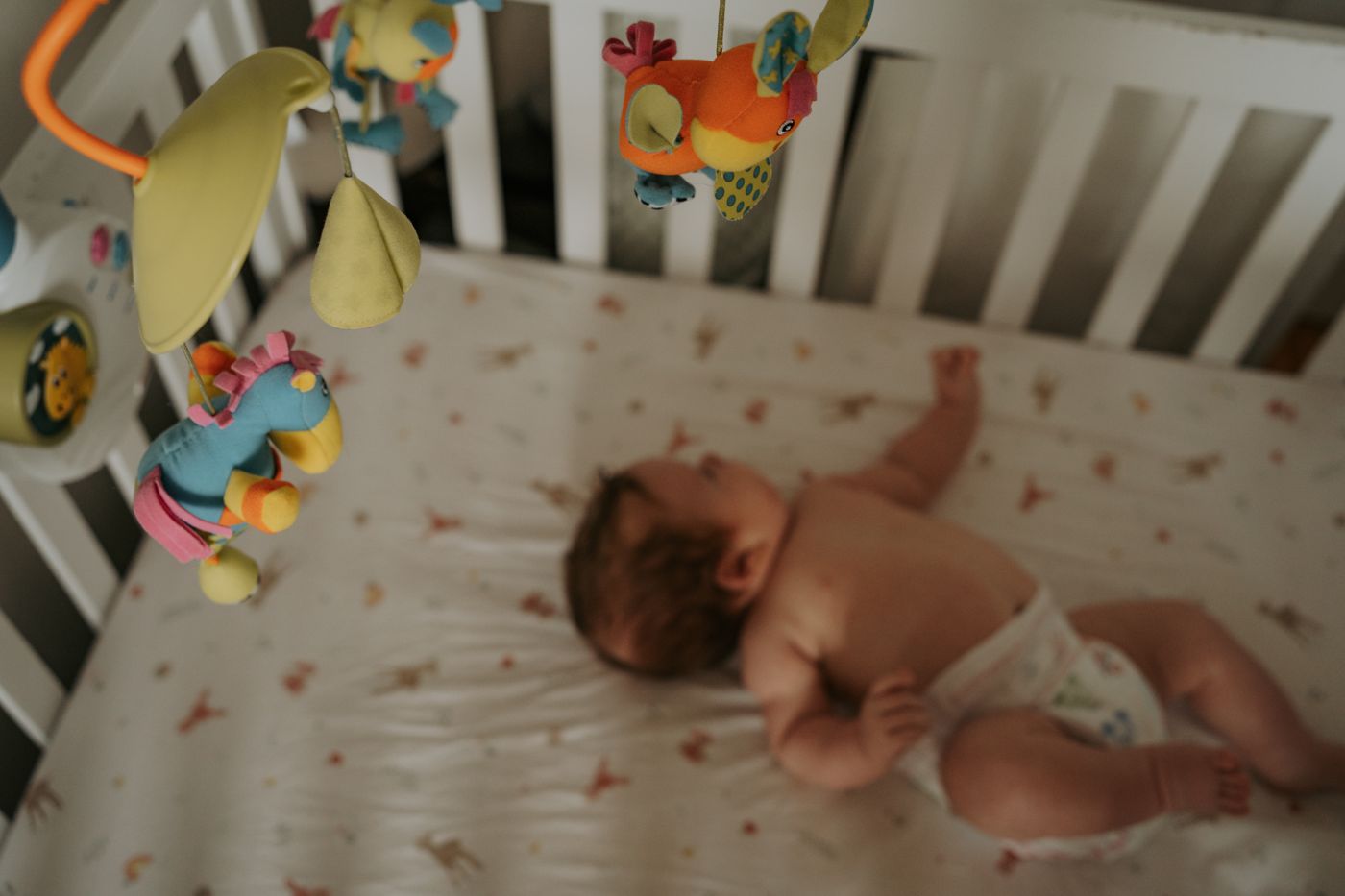 Newborn in the crib beneath a colourful mobile