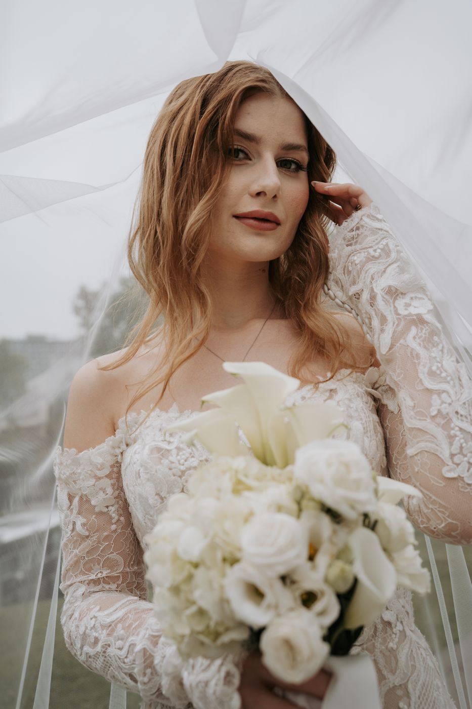 Bride under her veil holding a white calla lily bouquet