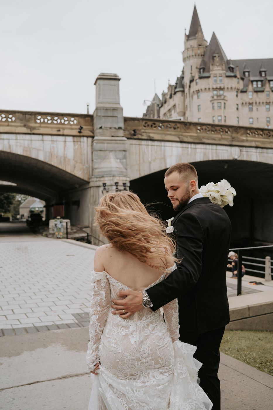 Bride and groom walking by the Rideau Canal beneath the Château Laurier in Ottawa