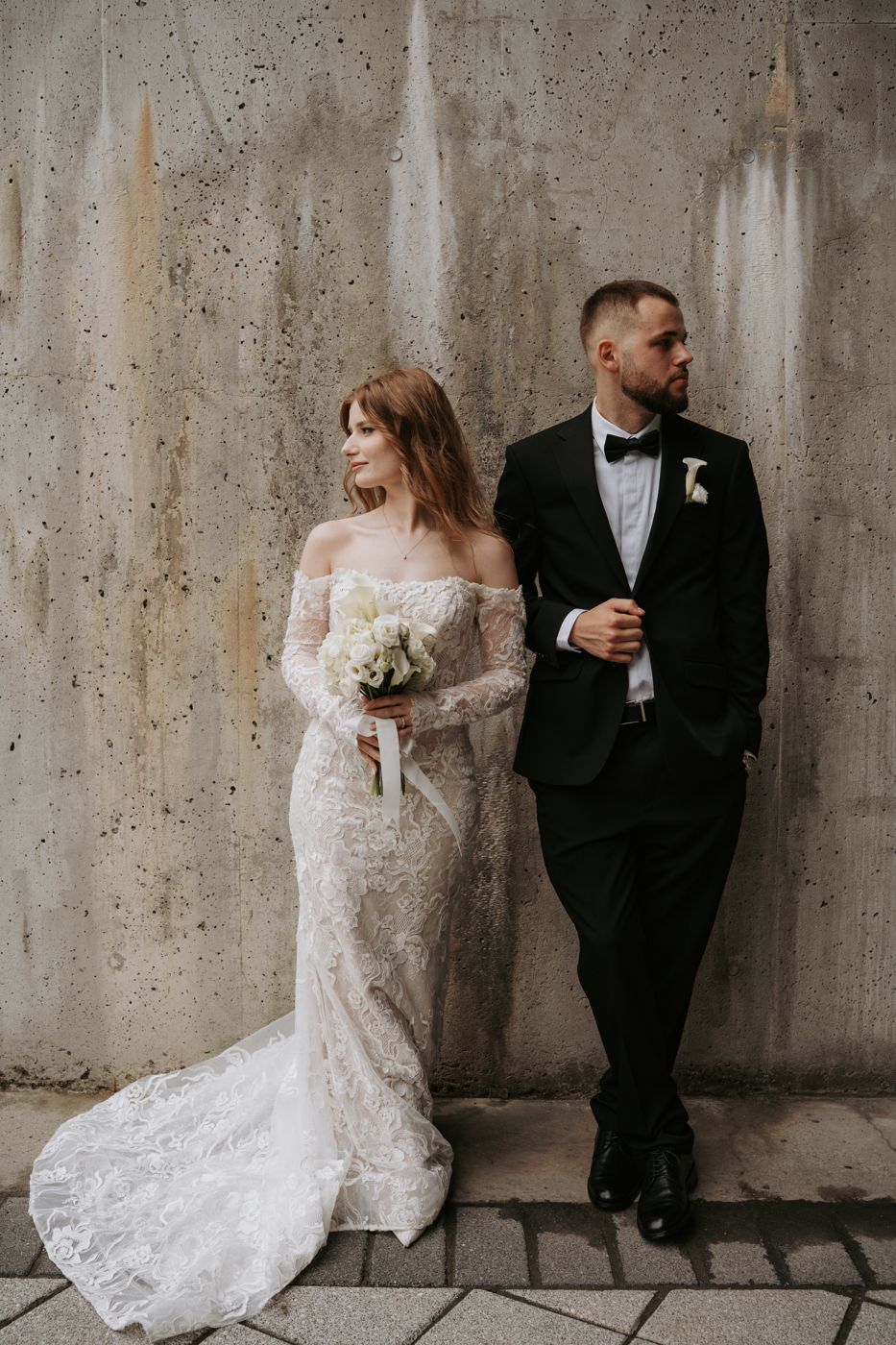 Bride and groom leaning on a concrete wall