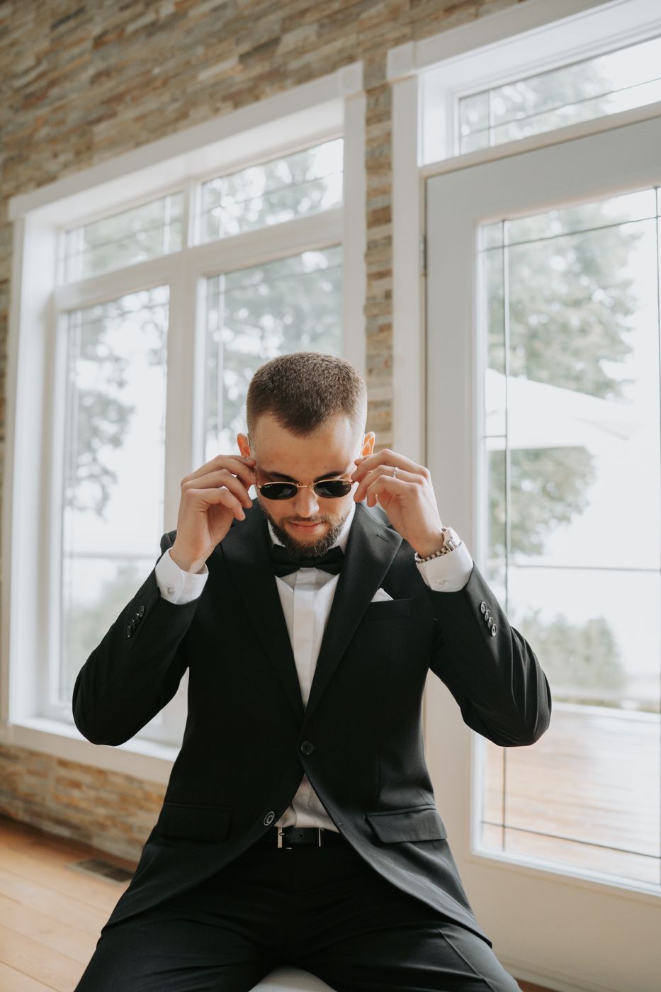 Groom putting on sunglasses by the window while getting ready